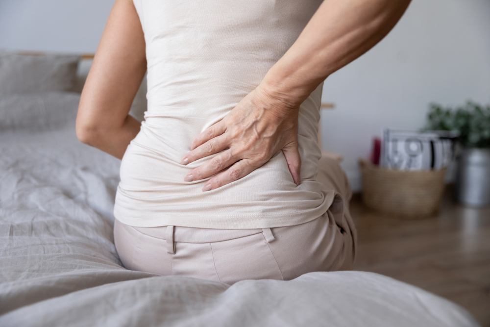 mature woman suffering from lower spine pain sitting on bed