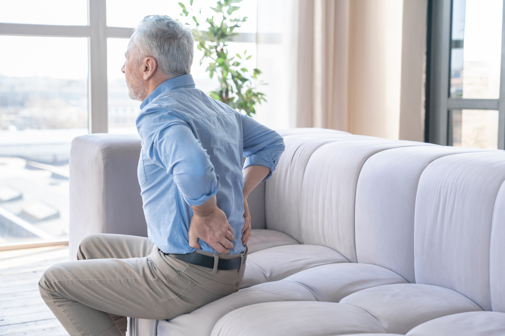 Man sitting on couch with severe back pain.